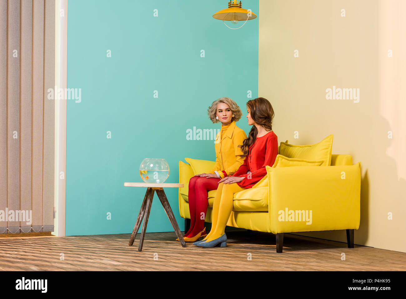 Im Retrostil Frauen sitzen auf gelben Sofa mit Aquarium Fische auf dem  Couchtisch bei farbenfrohes Apartment, Puppenhaus Konzept Stockfotografie -  Alamy