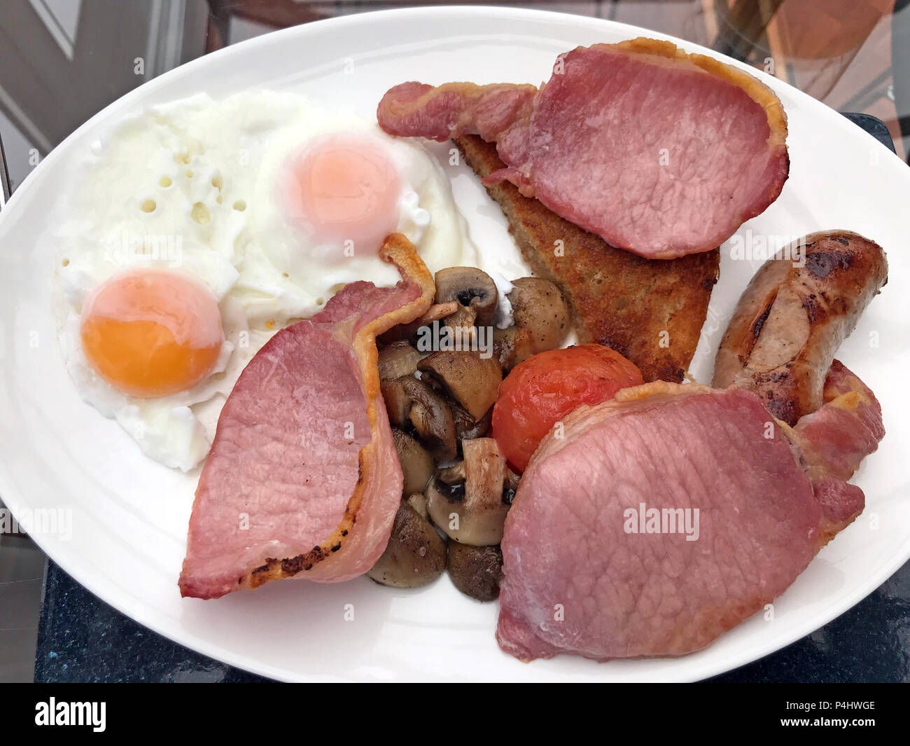 Englisches warmes Frühstück, gebratene Eier, Würstchen, gebratener Speck, Pilze, Tomaten, gebratenes Brot, auf einem Teller Stockfoto
