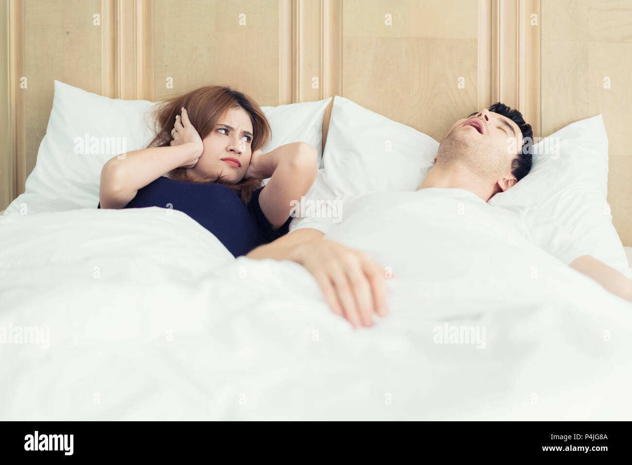Verärgert asiatische Frau blockieren Ihre Ohren vor Lärm von Mann Schnarchen im Schlafzimmer zu Hause. Junge Paare haben Probleme mit dem Schnarchen. Stockfoto