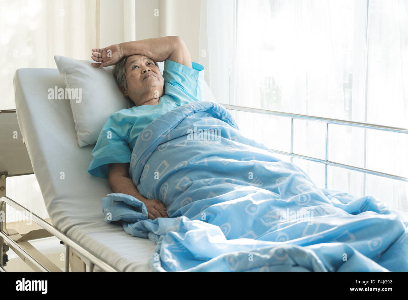 Asiatische gedrückt ältere Frau Patienten liegend auf Bett Blick aus dem Fenster im Krankenhaus. Ältere Frau Patienten ist froh, von der Krankheit erholt. Stockfoto