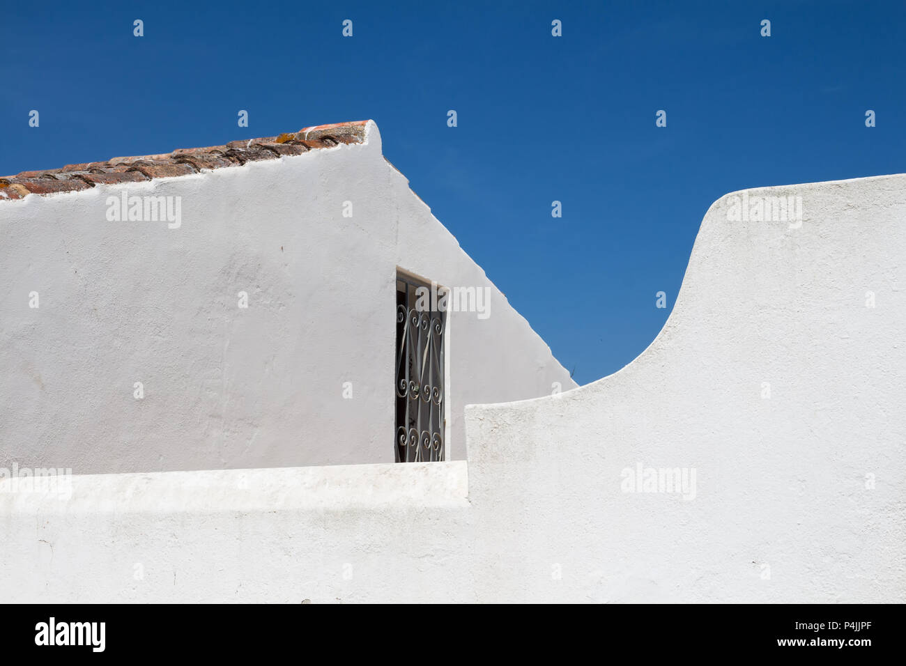 Weißer Fassade einer Kirche der Nossa Senhora da Rocha in Porches, Algarve, Portugal. Kante eines Daches. Fenster mit einem Gitter. Strahlend blauen Himmel. Stockfoto