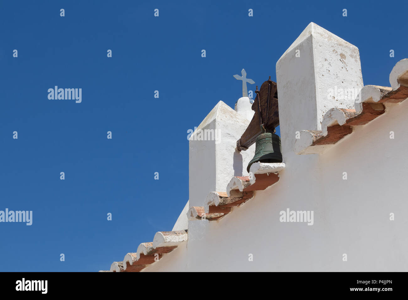 Diagonale Komposition von ein Detail einer weißen Kirche der Nossa Senhora da Rocha in Porches, Algarve, Portugal. Glockenturm, Rand von einem Dach und einem Kreuz. Hell Stockfoto