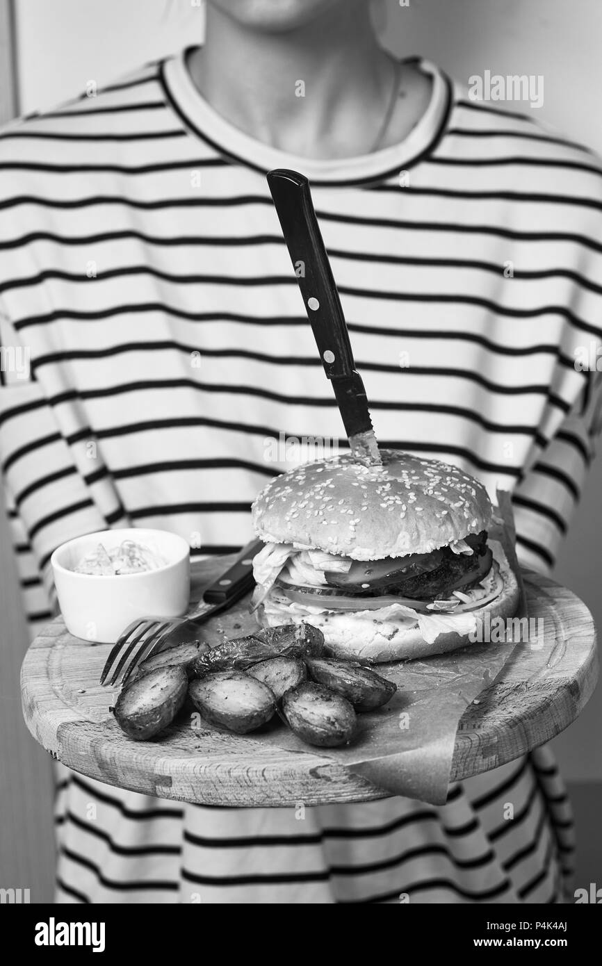 Frau gekleidet in gestreiften Pullover Holding runde Holzplatte mit appetitlichen Beteiligung mit Kirschtomaten, Rosmarin und Sauce liegen auf Stück von Kra serviert. Stockfoto