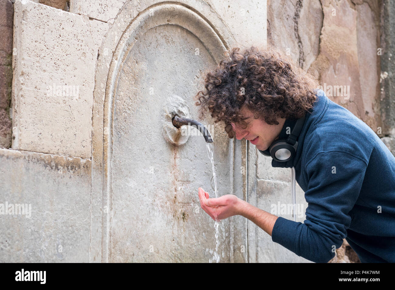 Hübsche junge Mann mit lockigem Haar Trinkwasser aus einem Brunnen Stockfoto