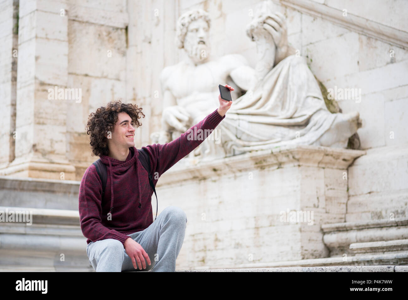 Hübscher junger Mann mit lockigem Haar in Trainingsanzug unter selfie mit seinem Handy vor Nil Gott Statue in Rom Stockfoto