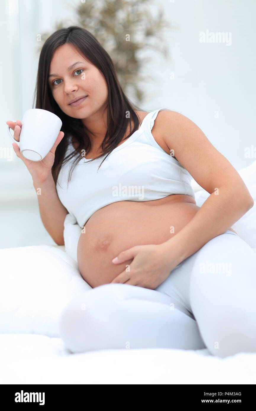 Glücklich schwanger Frau trinkt Milch im Wohnzimmer sitzen. Stockfoto