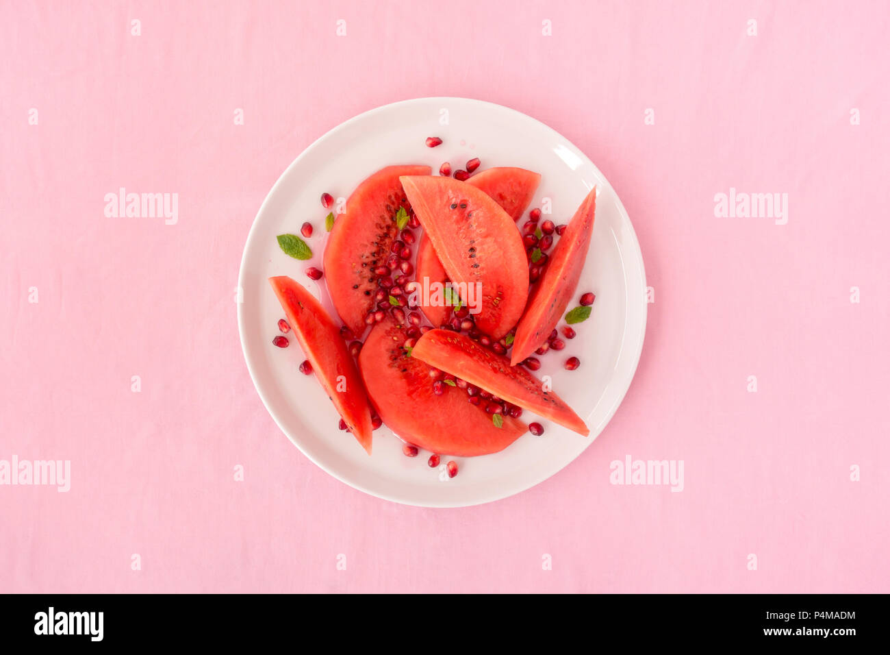 Wassermelone und Granatapfel Salat auf einem weißen Teller und rosa Stoff Hintergrund. Stockfoto