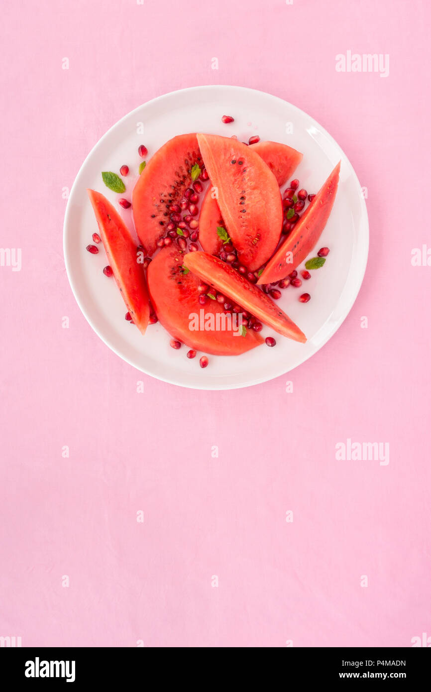 Wassermelone und Granatapfel Salat mit Minze auf einer weißen Platte und rosa Tischdecke eingerichtet. Stockfoto