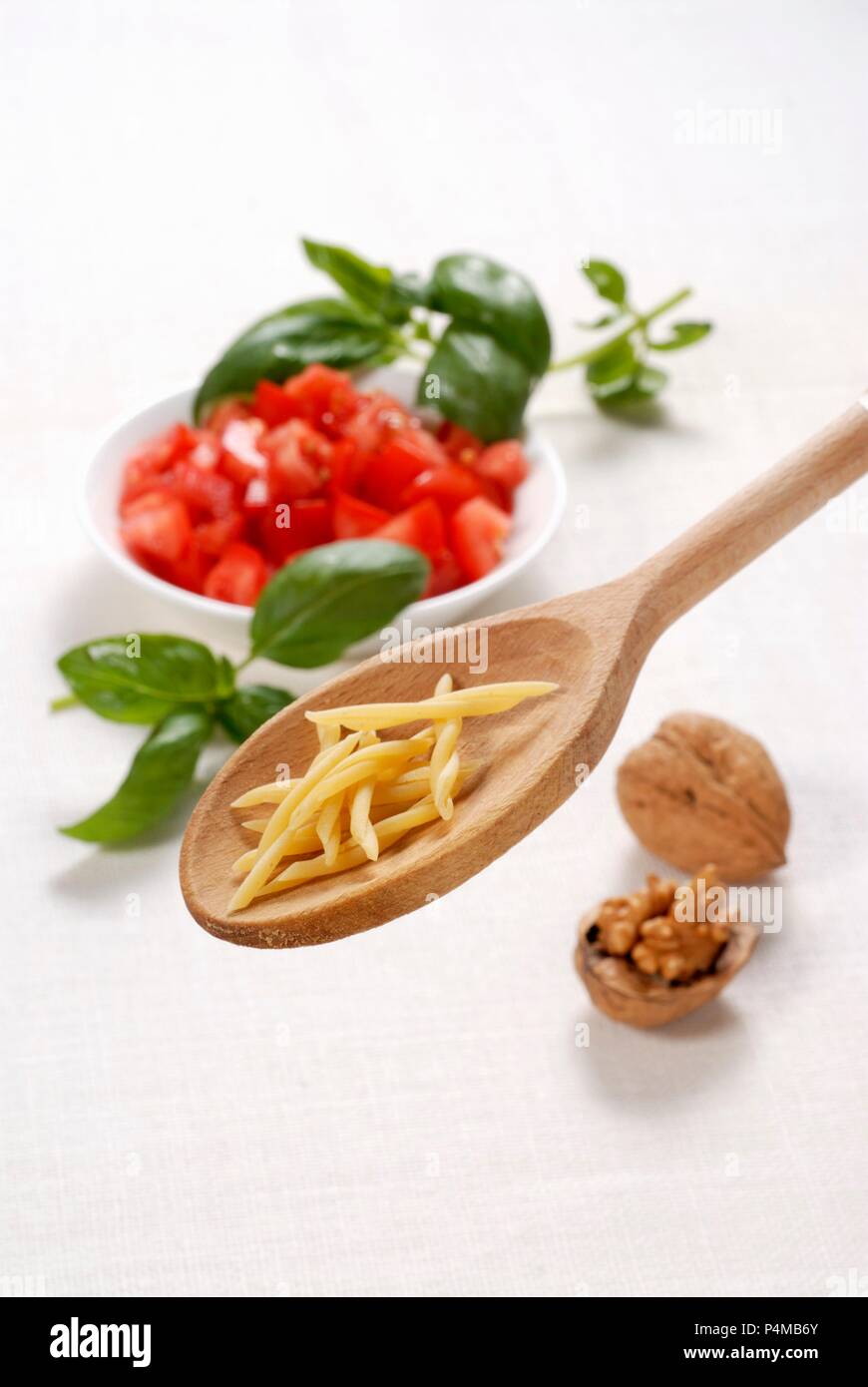 Strozzapreti auf einem Löffel aus Holz mit Tomaten, Basilikum und Walnüsse Stockfoto