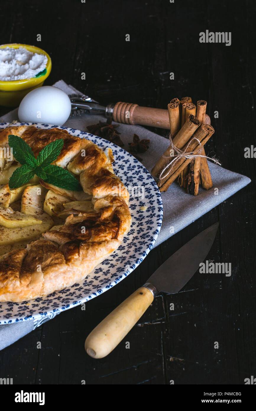 Apfelkuchen auf Platte, mit Zimt, Eier und Puderzucker im Hintergrund Stockfoto