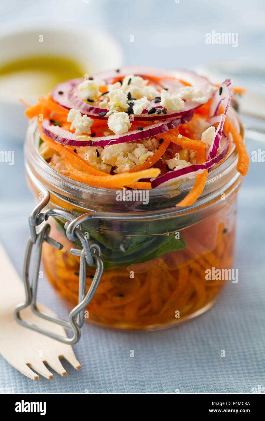 Karottensalat mit Muttern, Feta, Spinat, roten Zwiebeln, Olivenöl und schwarzem Sesam in einem Marmeladenglas Stockfoto