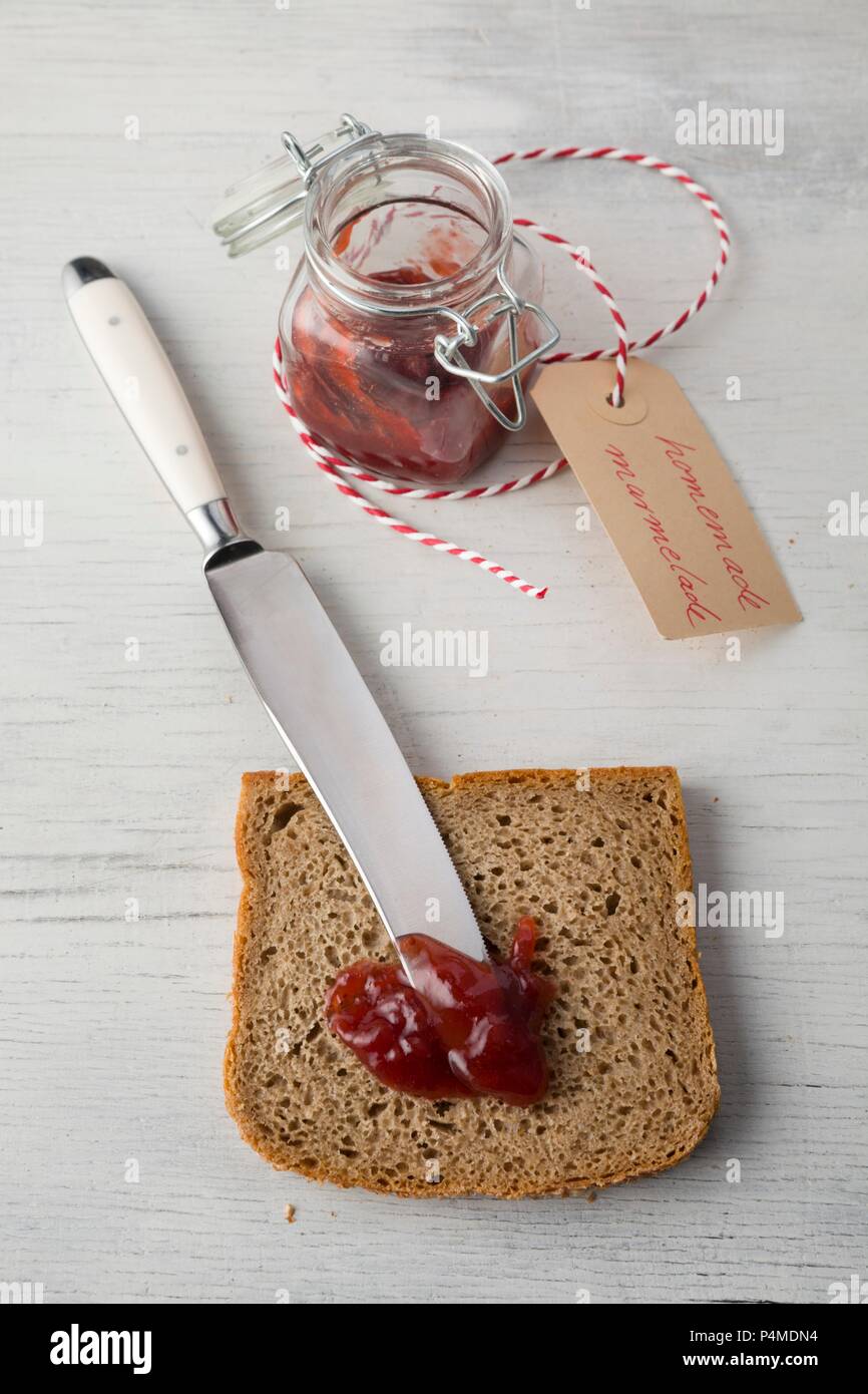 Eine Scheibe Roggenbrot mit einem Messer und Erdbeermarmelade Stockfoto