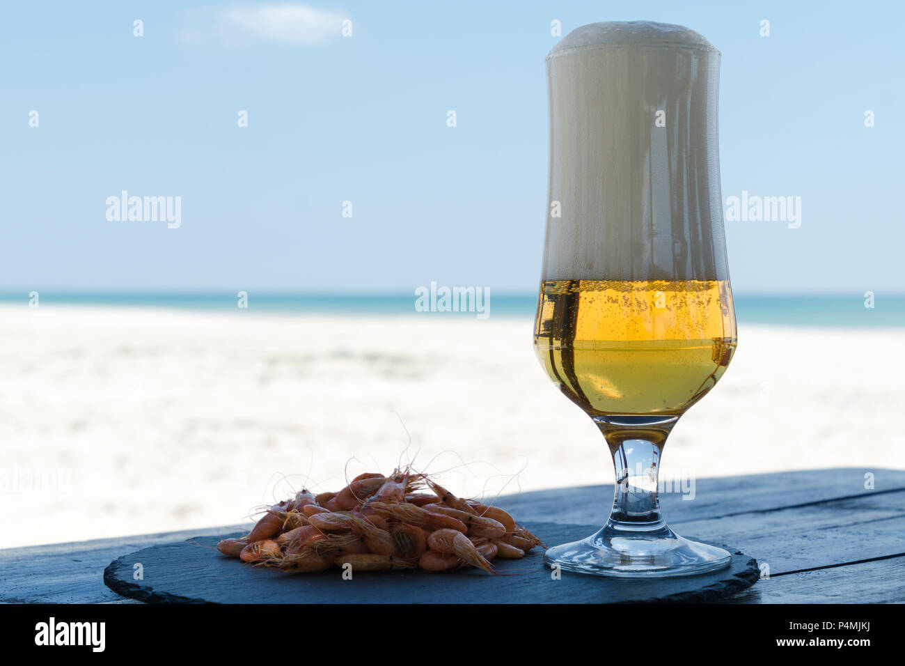 Bier Glas und Garnelen auf der Steinplatte im Schatten Tabelle gegen Sunny Beach verschwommenen Hintergrund des Meeres Stockfoto