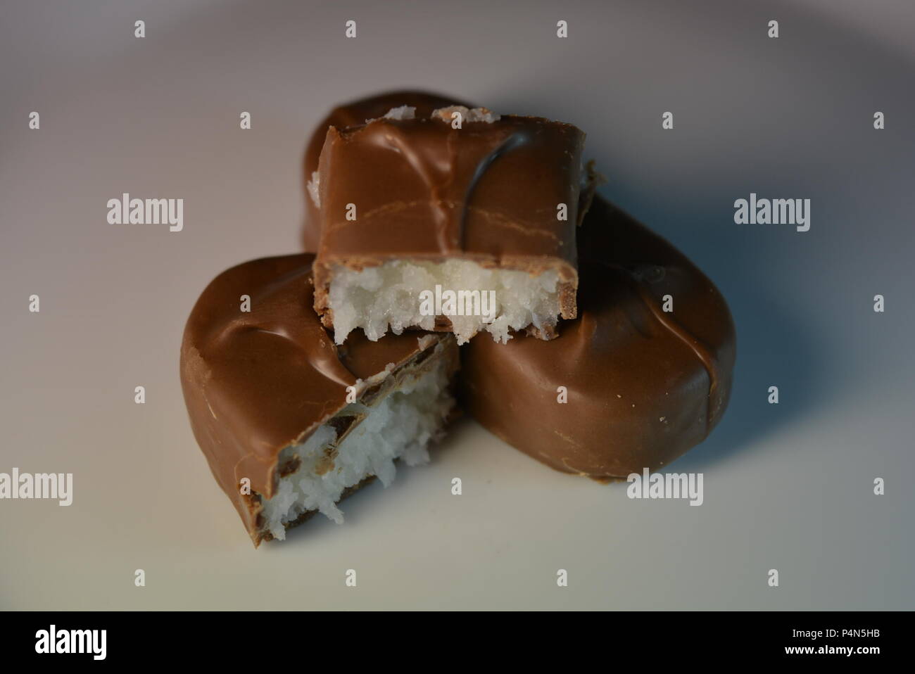Stücke, Scheiben süßer Kokosnussriegel bedeckt mit Milchschokolade auf einer weißen Glasplatte. Stockfoto