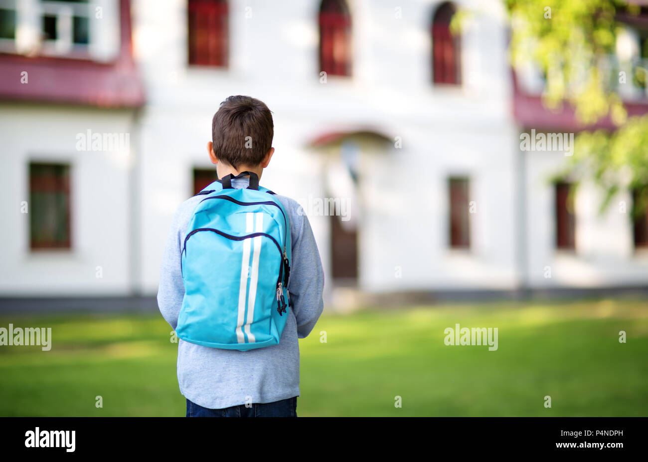 Junge mit Rucksack infront von einem Schulgebäude Stockfoto