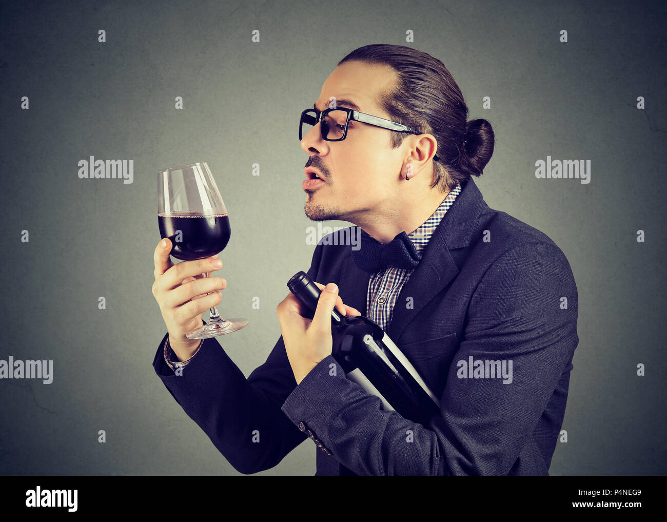 Formale ironische Mann mit Flasche und Glas Rotwein mit Liebe zum Alkohol auf grauem Hintergrund Stockfoto
