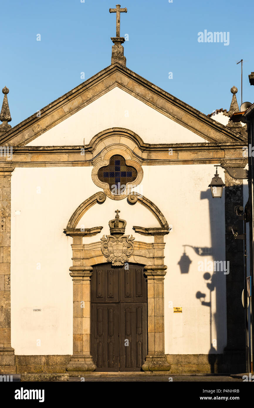 Tür mit geschwungenen Giebel und Stein Wappen oben, und Schatten der Stadt Licht an der Wand. Igreja da Misericordia Kirche, Trancoso, Portugal. Stockfoto