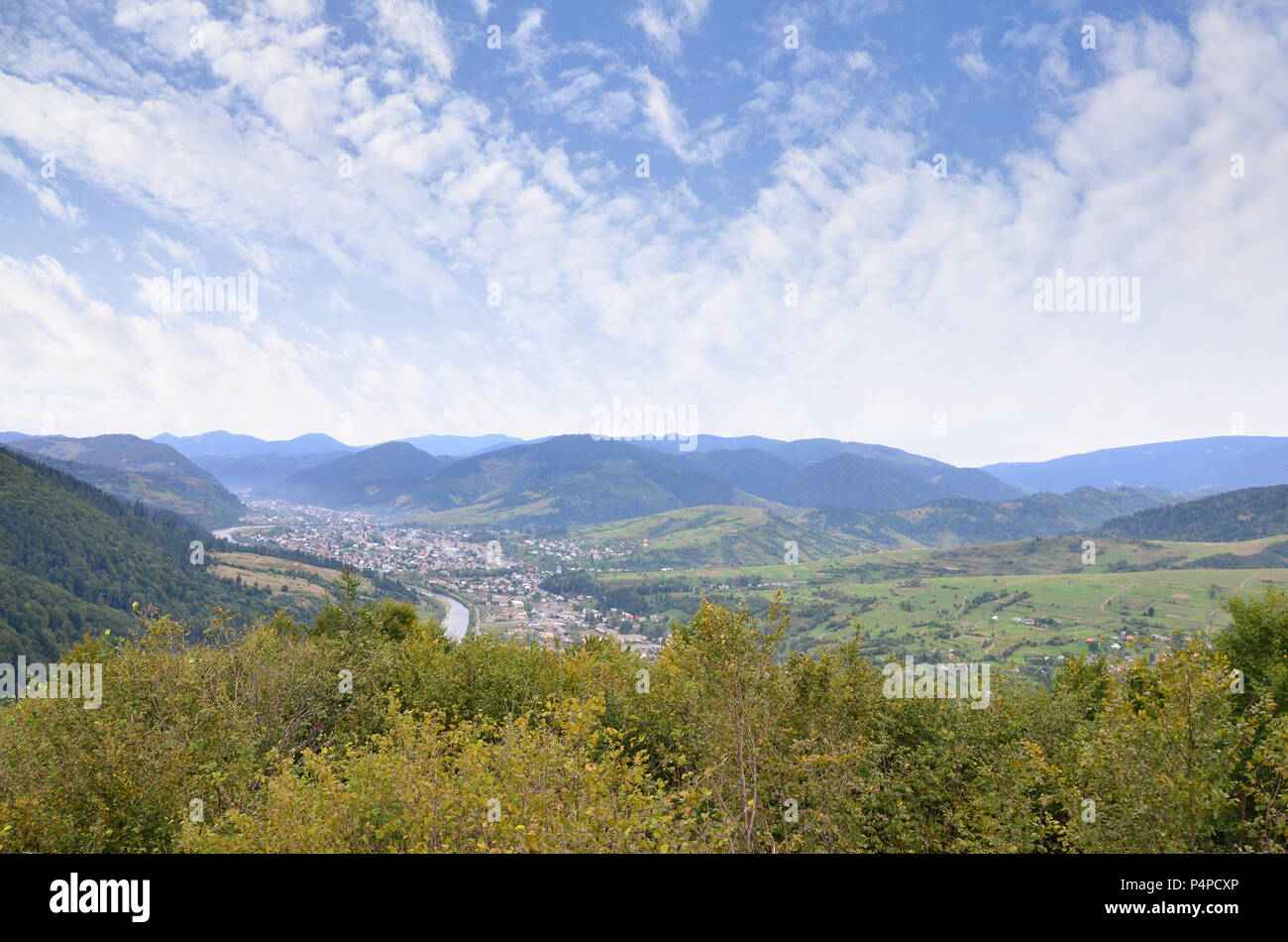 Eine wunderschöne Aussicht auf das Dorf Mezhgorye, Karpaten Region. Eine Menge von Wohngebäuden durch hohe Wald Berge und lange Fluss umgeben. Stockfoto