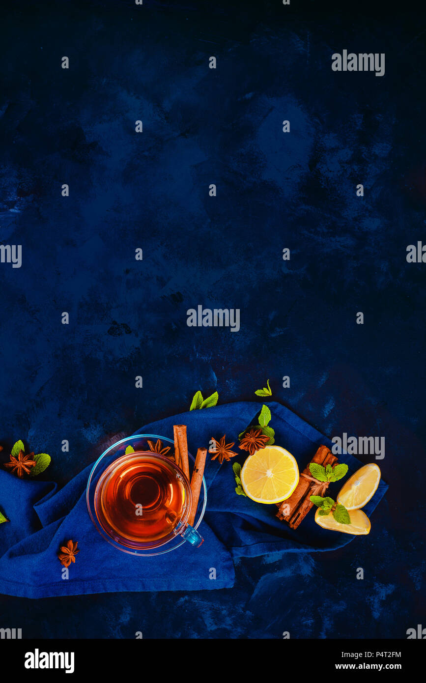 Glas Tee Tasse und Untertasse mit Zitronenscheiben, Zimt, Anis Sterne und Minze auf einem dunklen Hintergrund mit Bettwäsche Serviette. Lebendige Farben heißen Getränk fla Stockfoto