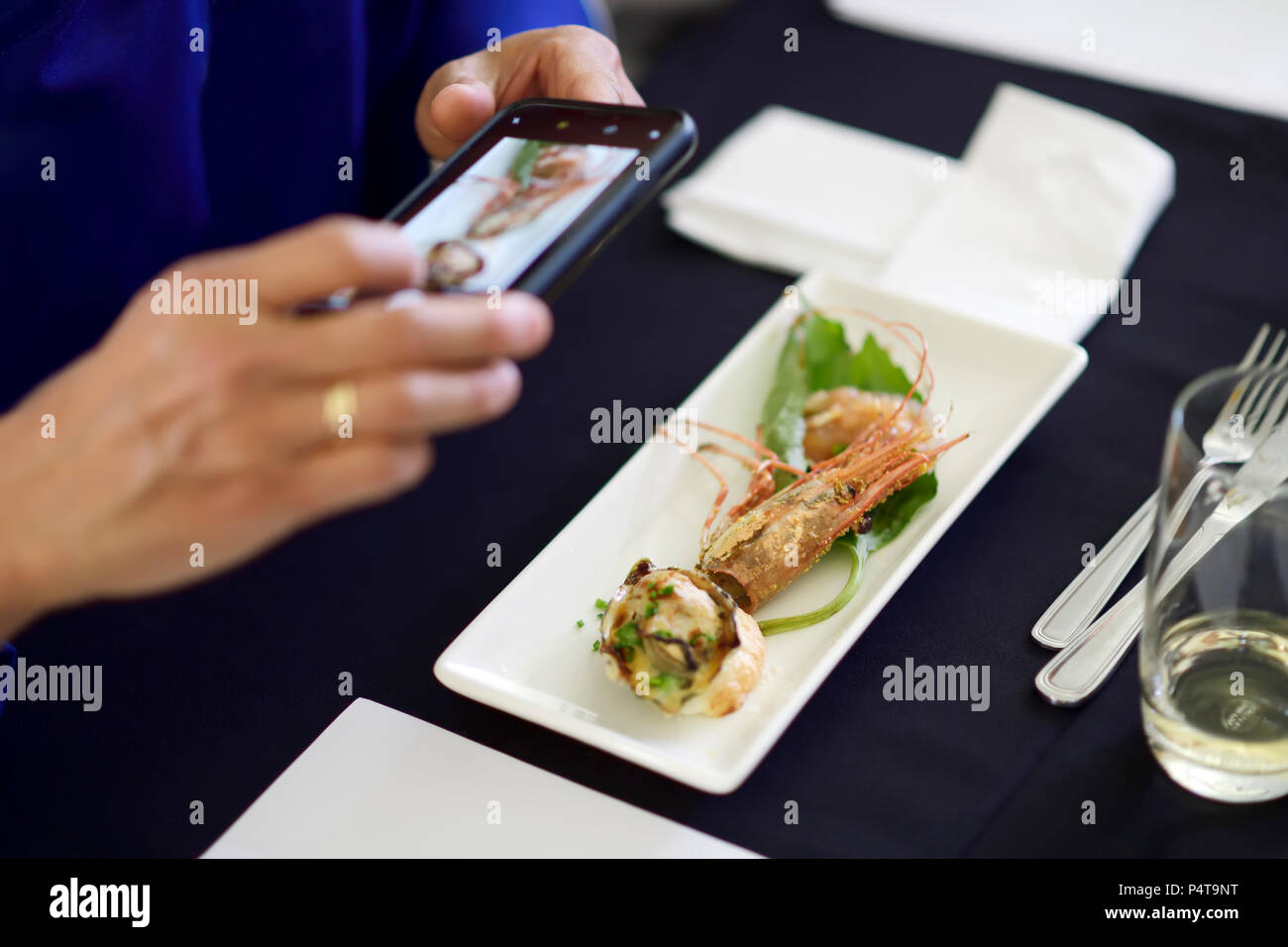 Nahaufnahme der Hand einer Person mit einem Smartphone Aufnahmen von einem Gourmet Meeresfrüchte essen in einem Restaurant Stockfoto