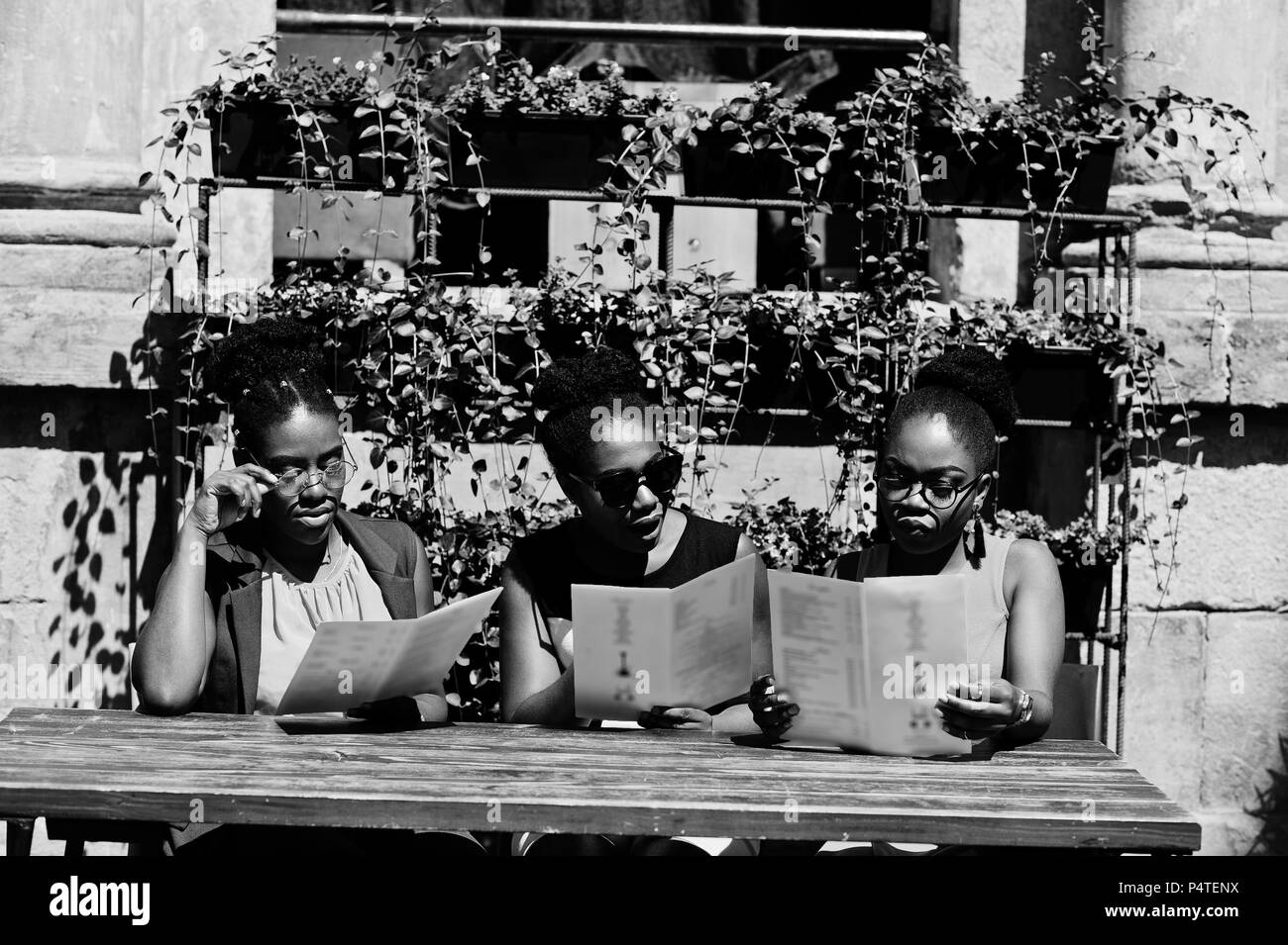 Drei stilvollen afrikanischen amerikanischen womans an sonnigen Sommertag im Freien, sitzen am Tisch des Restaurants mit Speisekarte in Händen. Stockfoto