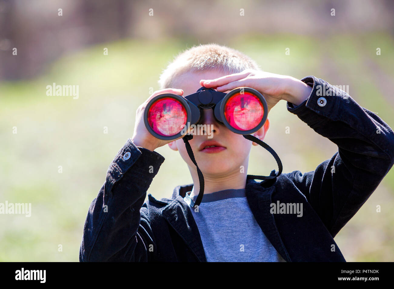 Portrait von kleinen niedlichen stattlichen cute blonde Junge aufmerksam beobachten, etwas durch ein Fernglas in der Entfernung auf einer verschwommenen Hintergrund. Kinder Unschuld, Stockfoto