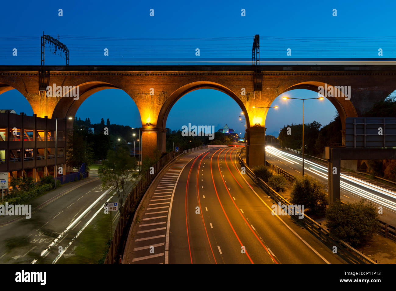 Die Autobahn M60 verläuft unterhalb der Stockport Eisenbahnviadukt wie ein Zug fährt in der Nacht. Stockfoto