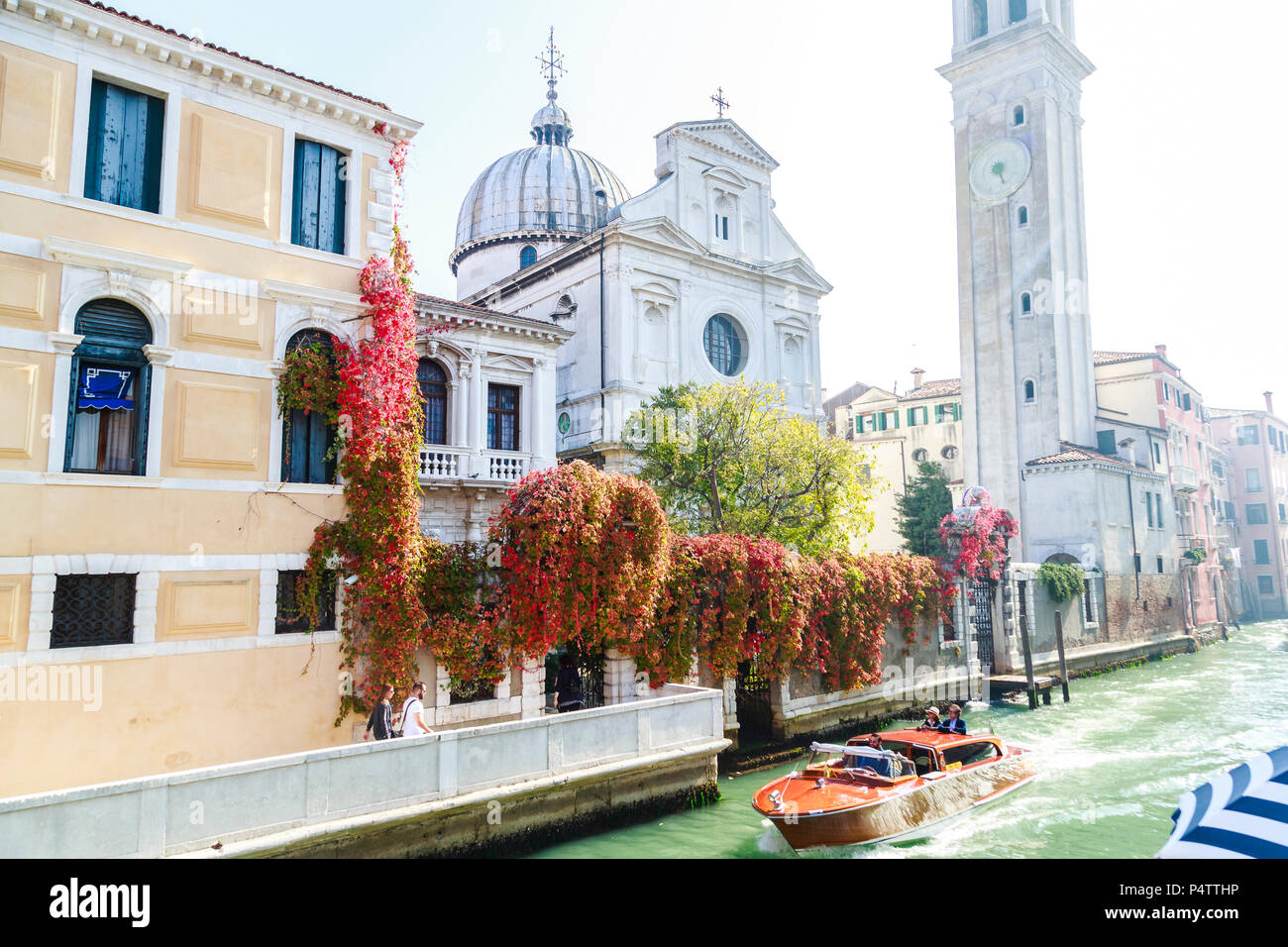 Klassische Motorboot mit zwei ständigen Touristen und Geschäftsreisende, die Chiesa San Giorgio (Griechische Kirche) am Rio del Greci im hellen Sonnenschein und Farben, Venedig, Italien. Stockfoto