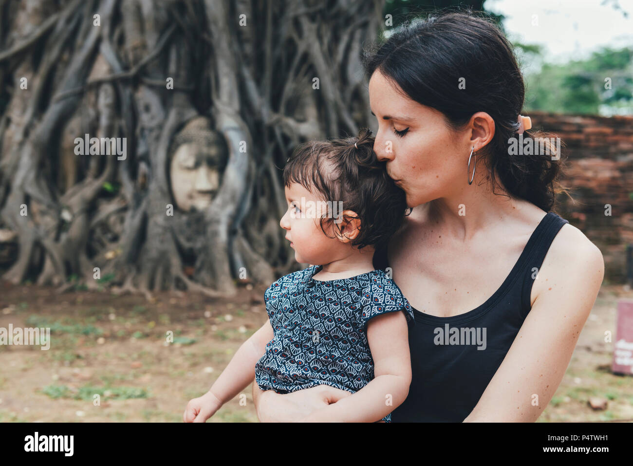 Mutter küssen Ihrer Tochter in Wat Mahathat Ayutthaya mit Buddha Kopf im Baum Wurzeln im Hintergrund Stockfoto
