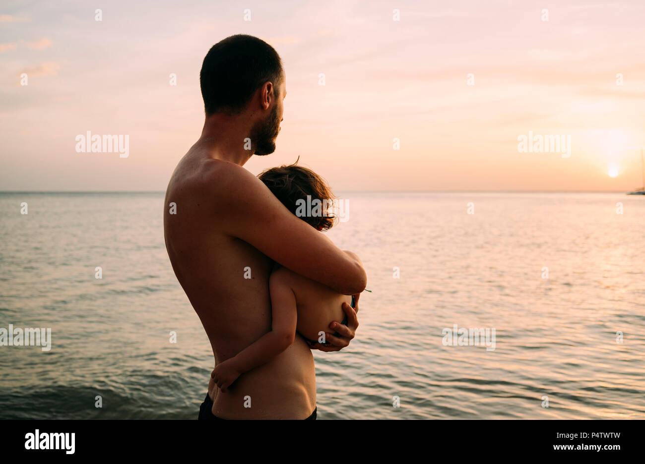 Vater, die kleine Tochter auf seinen Armen, während Sonnenuntergang gemeinsam am Meer Stockfoto