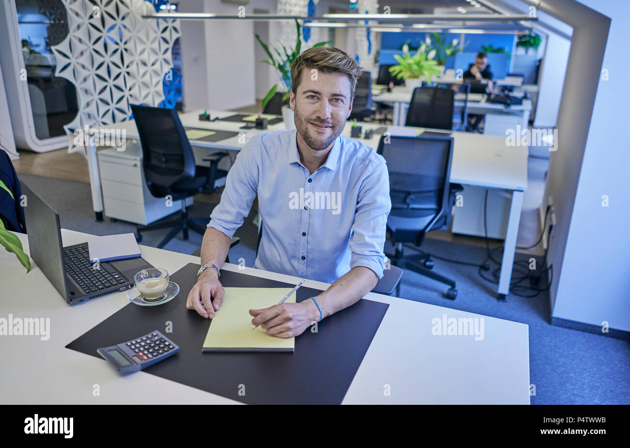 Portrait von lächelnden Geschäftsmann am Schreibtisch sitzen in open-plan Office Stockfoto