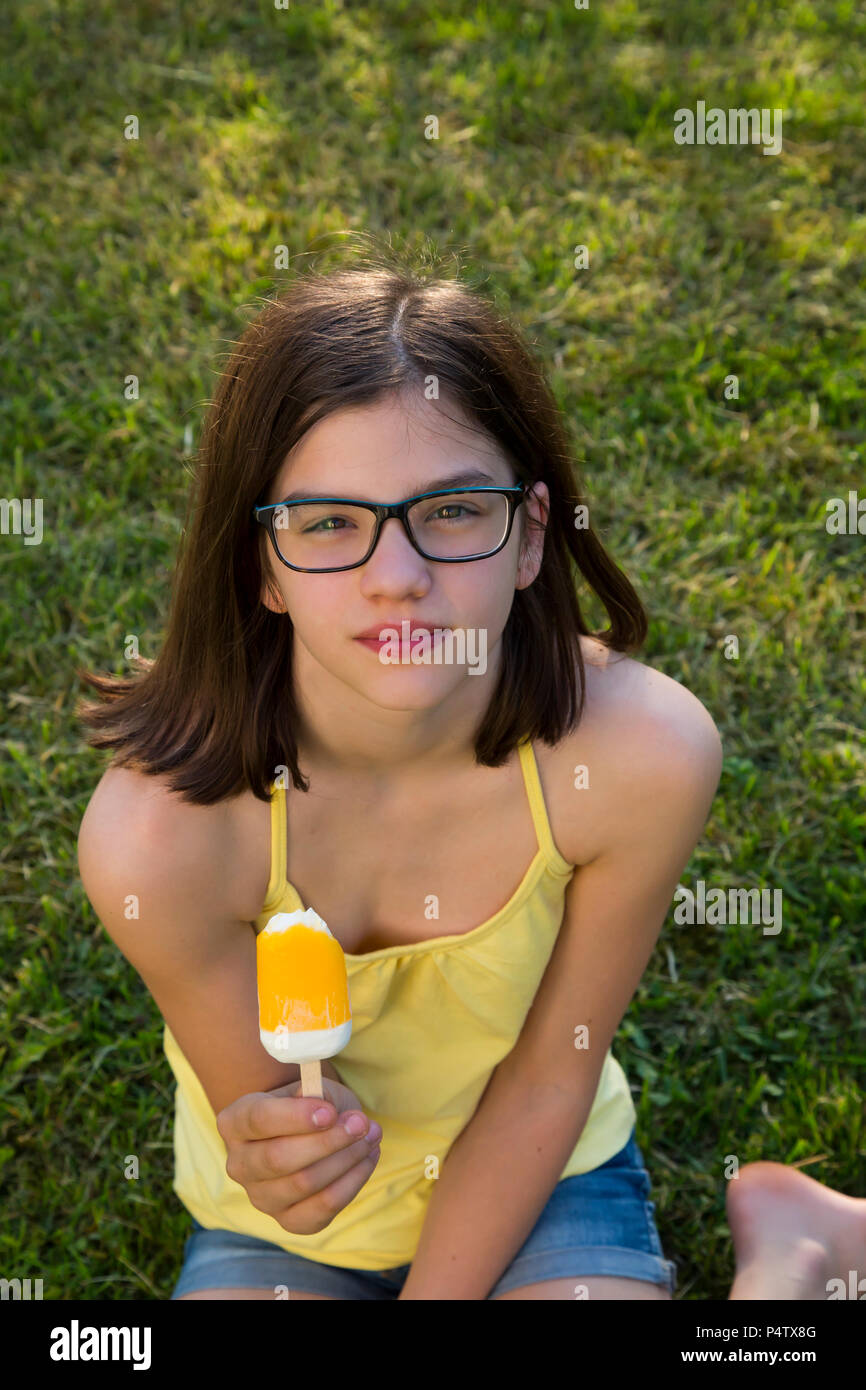 Portrait von Mädchen mit Brille sitzen auf einer Wiese Eis essen Lolly Stockfoto