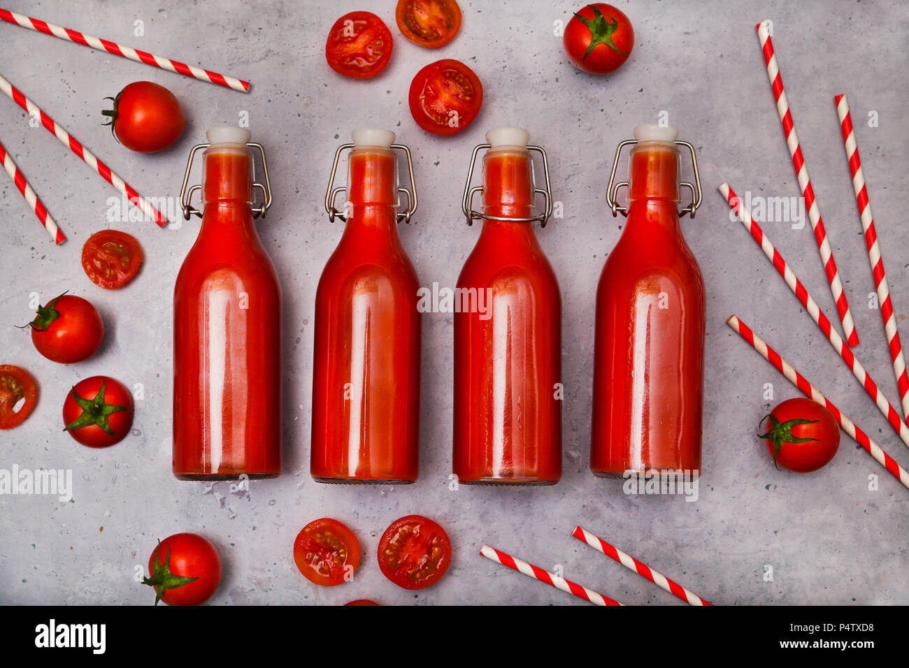 Reihe von vier Swing top Flasche hausgemachten Tomatensaft, Strohhalme und Tomaten auf grauem Grund Stockfoto