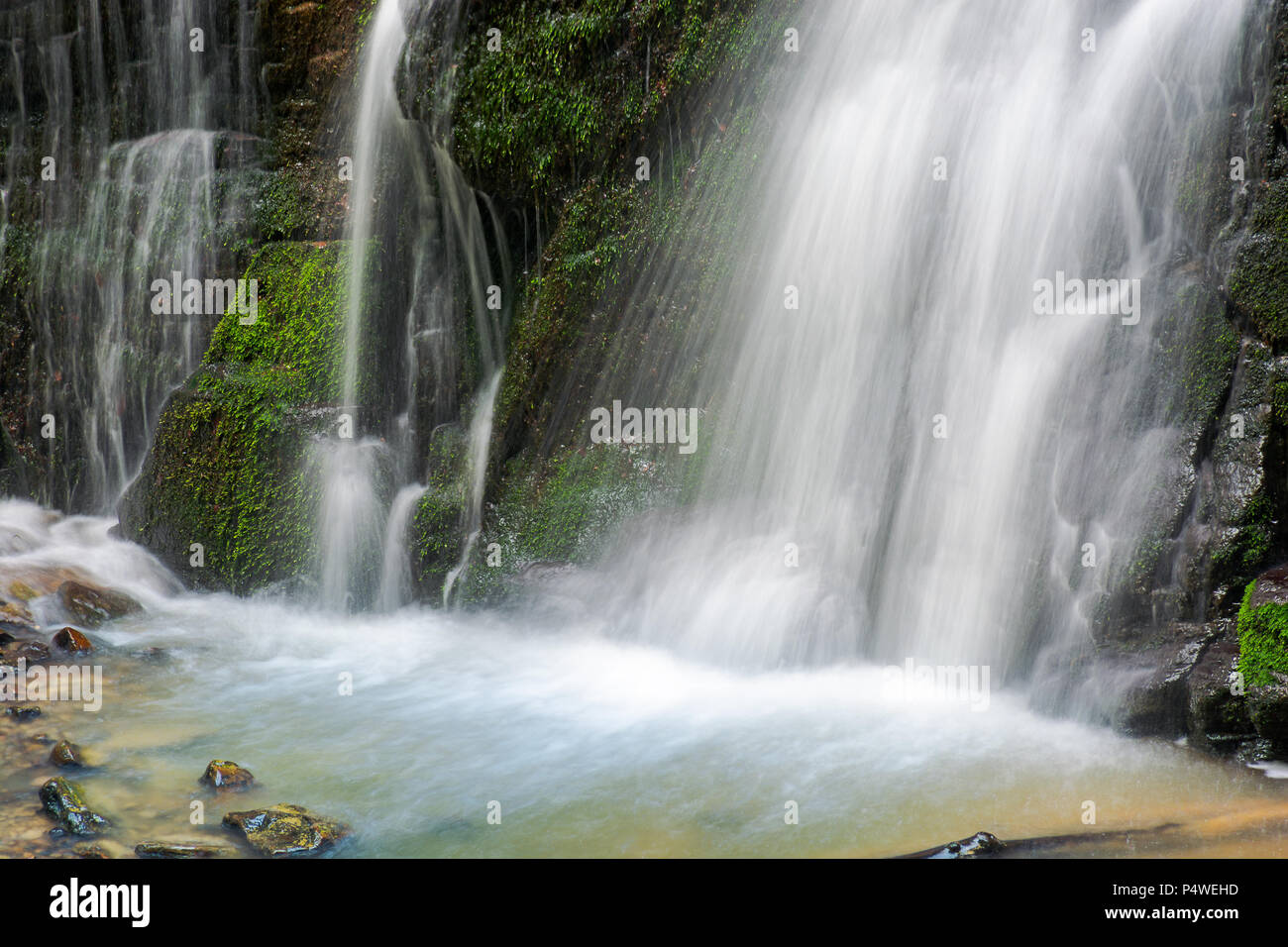 Nahaufnahme der Wasserfall Fuß mit bemoosten Felsen. schönen ruhigen Natur Hintergrund. Frische und Energie des Wassers. Klare Umwelt und Ressourcen Konzept Stockfoto