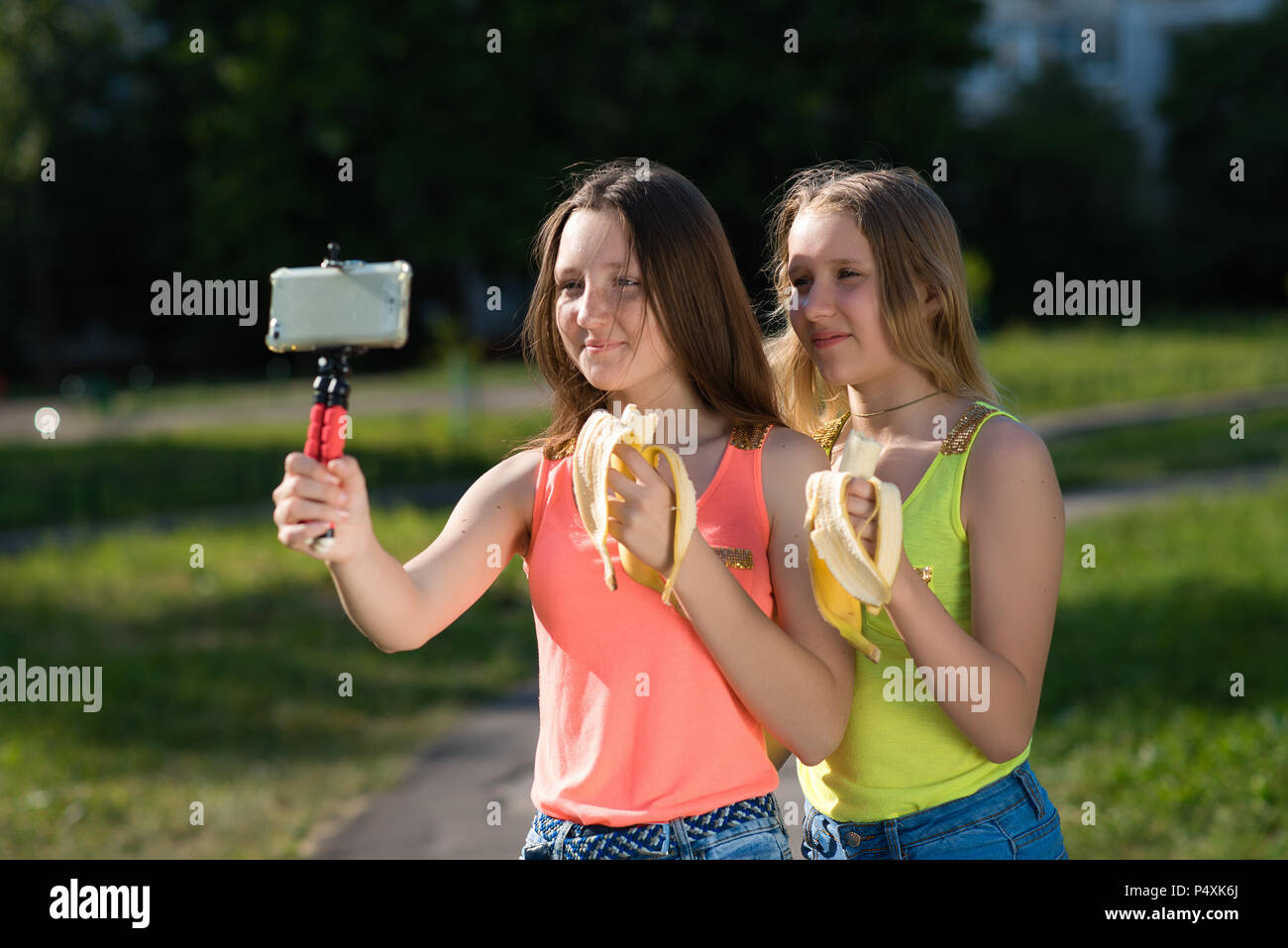 Zwei Mädchen Schülerin Freundinnen. Sommer in der Natur. In seinen Händen hält. Frisst Bananen. Das Konzept der junge Blogger. Emotionale glückliches Lächeln essen. Stockfoto