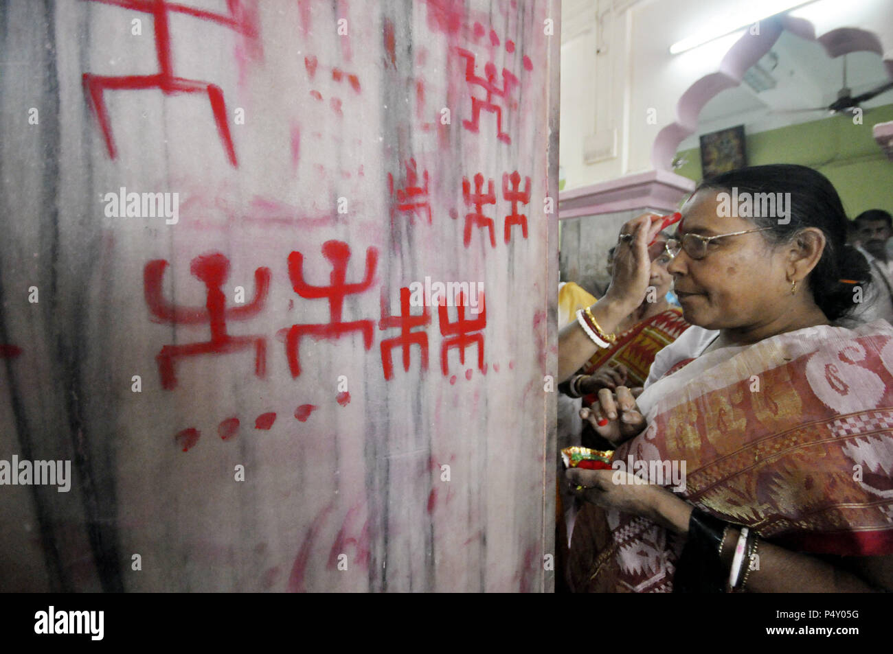 Eine indische Frau vermilion Anwendung auf Ihrem Gesicht während der Ambubachi Festival. Die Swastika ist eine geometrische Abbildung und einer alten religiösen Symbol, mit Zinnoberrot an der Wand des Tempels als Teil der Rituale des Ambubachi in Agartala, Hauptstadt des nordöstlichen Bundesstaat Andhra Pradesh, Indien gezogen wird. Stockfoto