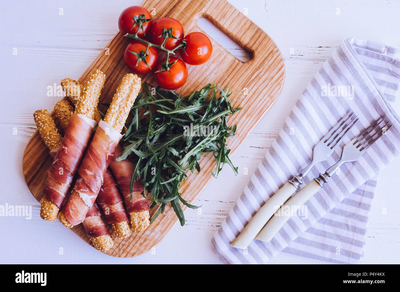 Grissini Brot Sticks mit Schinken und Rucola mit Tomaten auf Holzbrett ...