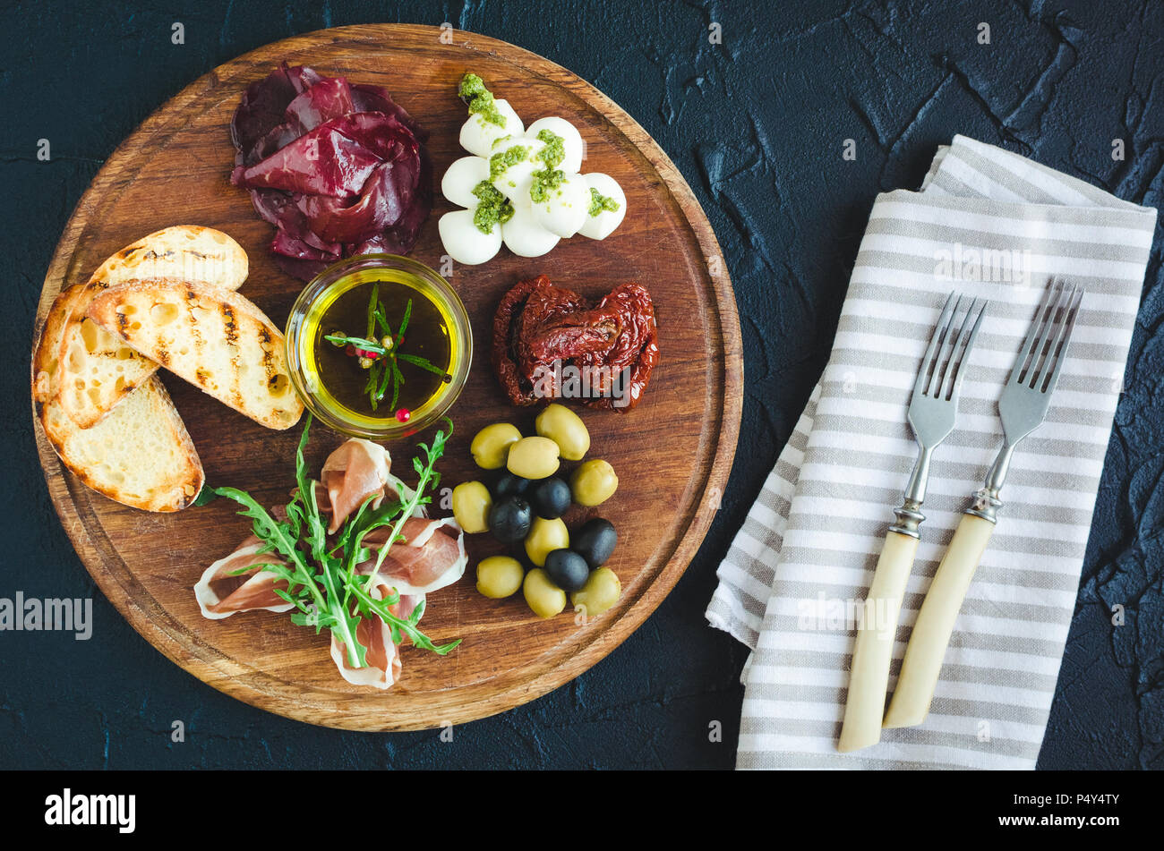 Auswahl an spanischen Tapas oder italienische Antipasti: Schinken, Bresaola, Mozzarella, getrocknete Tomaten, Oliven und Toast auf Holzbrett. Noch l Stockfoto