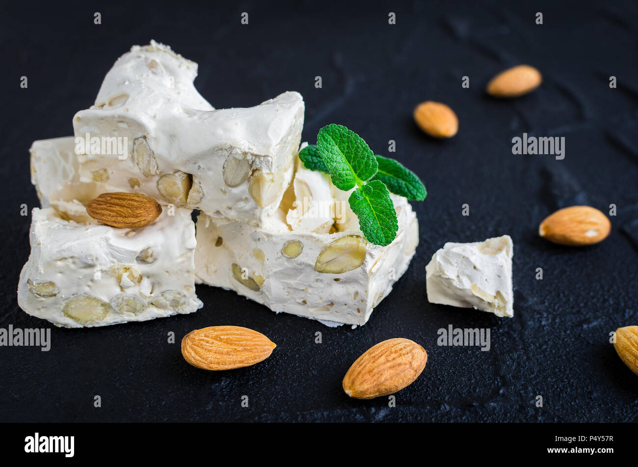 Süße Nougat mit Mandeln auf dem schwarzen Stein. Stücke von weißen Nougat. Stockfoto