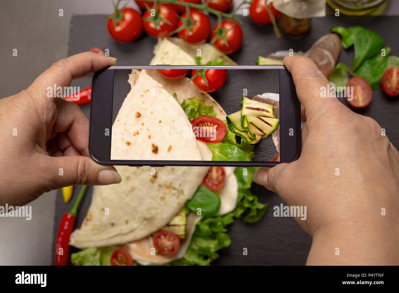 Der Aufnahme von Nahrungsmitteln mit Ihrem Smartphone für Instagram. Italienisches Piadina Romagnola Fladenbrot mit Salat, Tomaten, Schinken, mozzarel Stockfoto