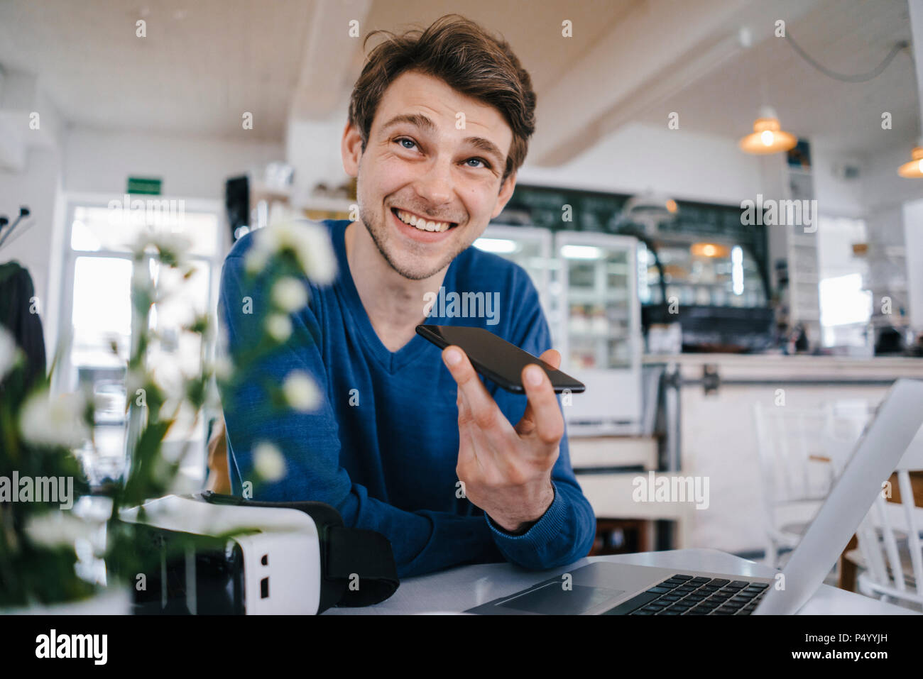 Lächelnd Mann in einem Café mit Handy und Laptop Stockfoto