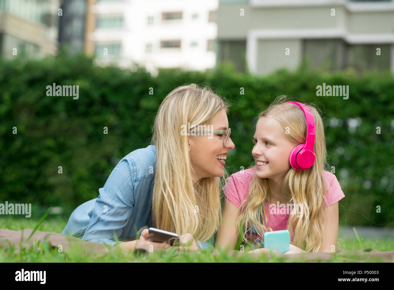 Glückliche Mutter und Tochter mit Smartphone und Kopfhörer im Garten Stockfoto
