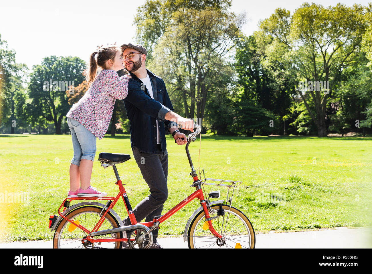 Tochter küssen Vater mit dem Fahrrad in einem Park Stockfoto