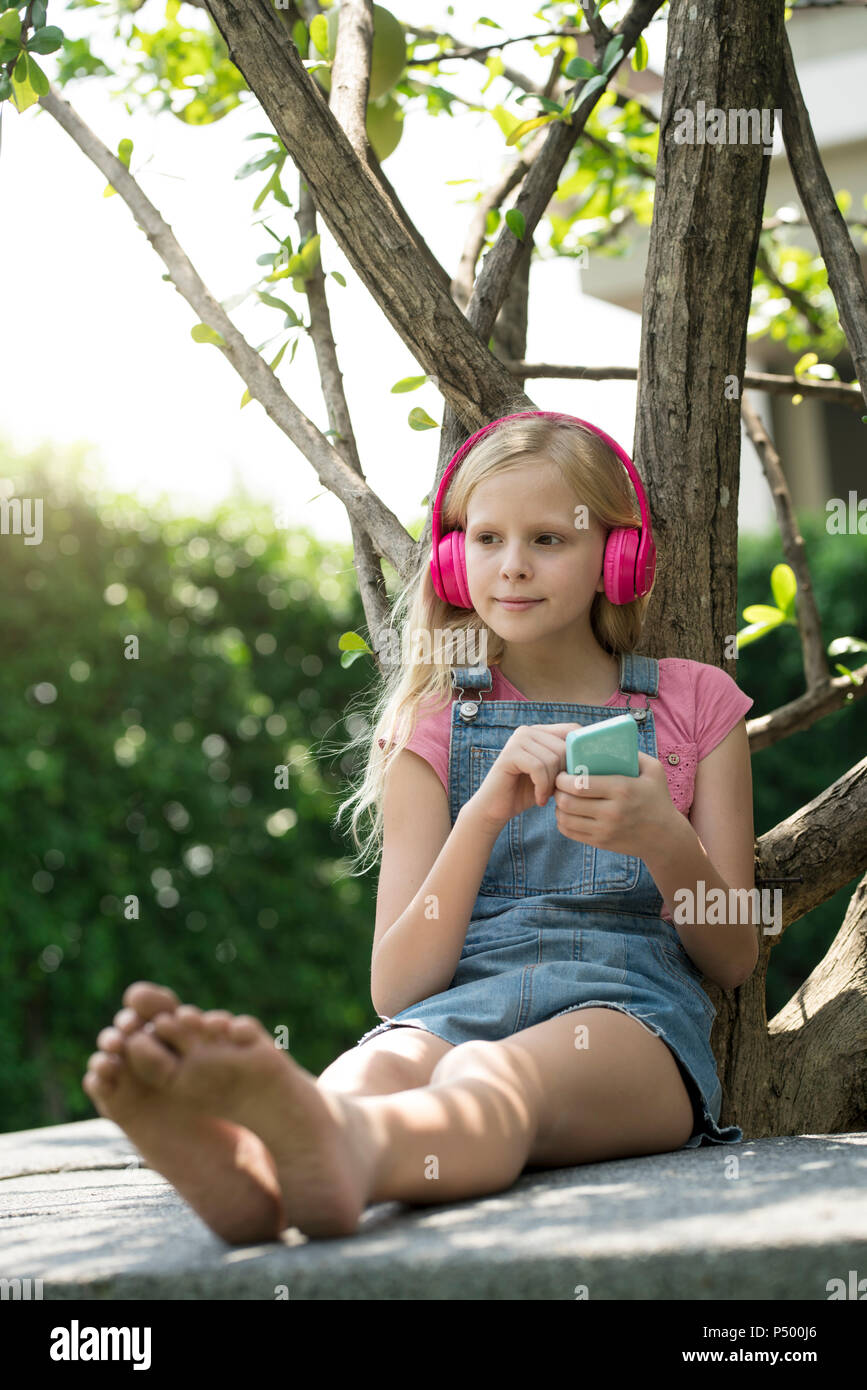 Süße blonde Mädchen Hören von Musik mit pink Kopfhörer im Garten Stockfoto