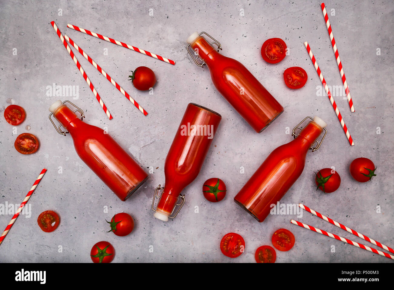 Hausgemachte Tomatensaft in Bügelflaschen, Strohhalme und Tomaten auf grauem Grund Stockfoto