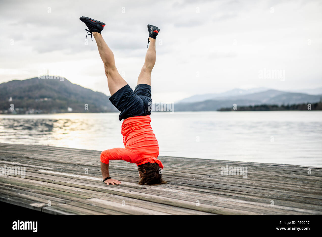 Sportler tun ein Kopfstand auf der Holzterrasse am Seeufer Stockfoto