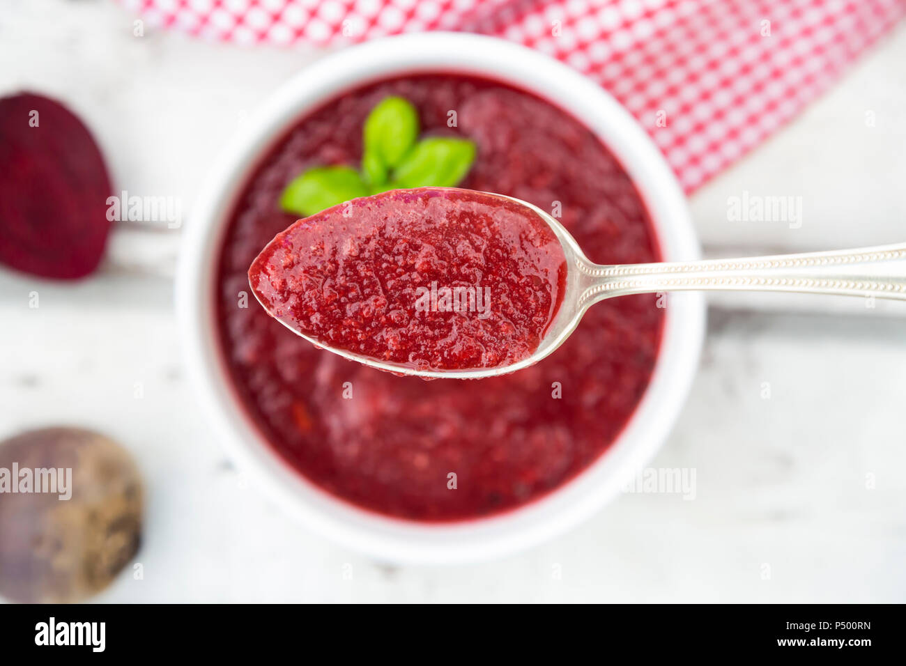 Rote-bete-Suppe auf Löffel, in Schüssel auf weißem Holz Stockfoto