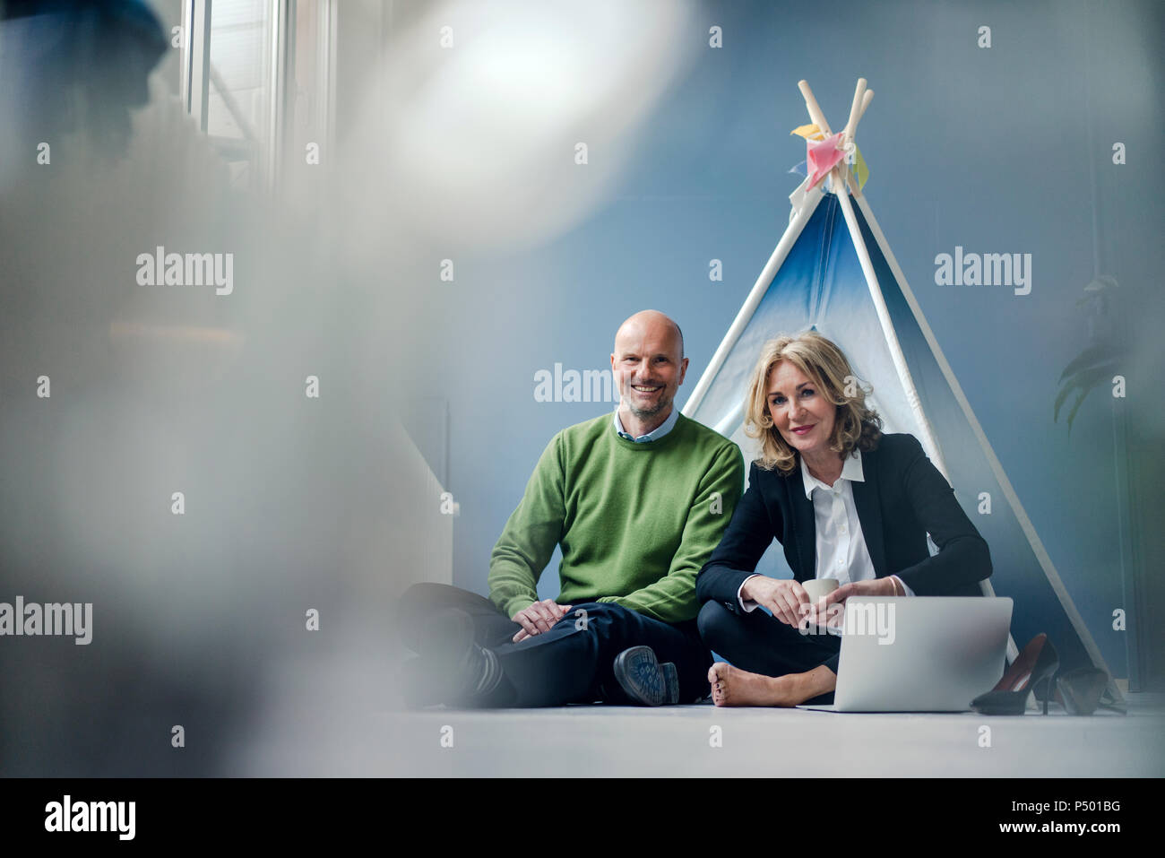 Lächelnd Geschäftsmann und Geschäftsfrau im Tipi drinnen sitzt mit Laptop Stockfoto