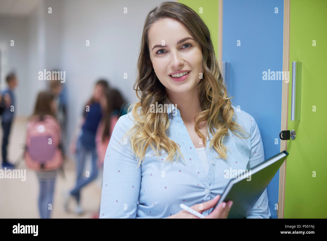Portrait von lächelnden Lehrer auf Korridor in der Schule mit Schülern im Hintergrund Stockfoto