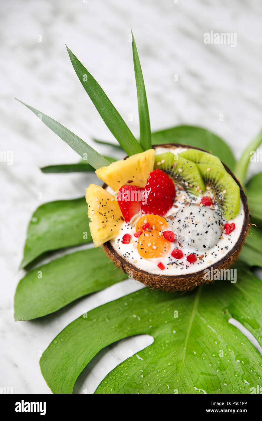Kokosnuss Schale mit Variuos Früchte, Joghurt und Samen auf Blatt Stockfoto